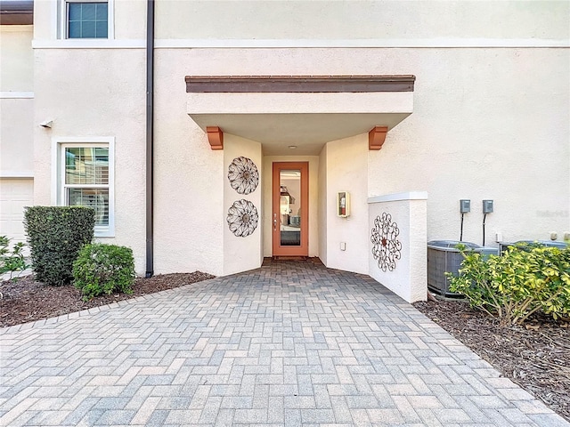 view of exterior entry featuring central air condition unit and stucco siding