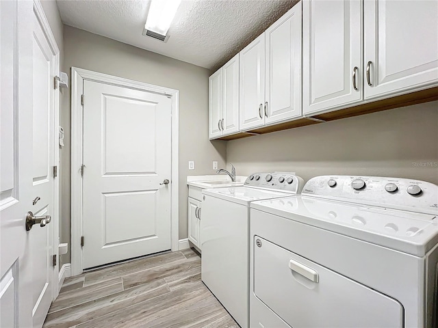 washroom with cabinet space, light wood-style flooring, a sink, a textured ceiling, and independent washer and dryer