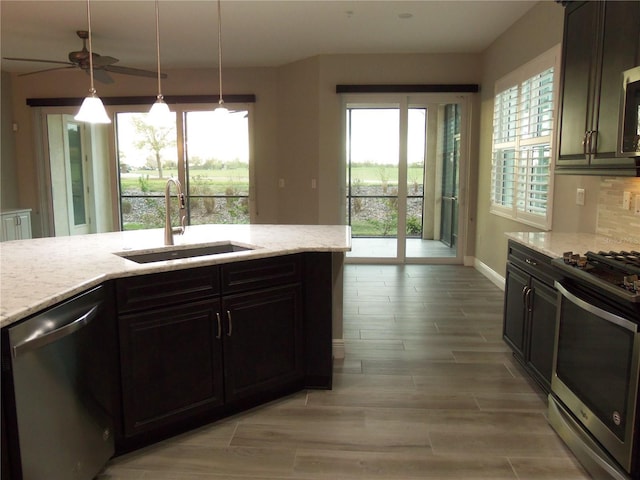 kitchen with stainless steel appliances, wood finish floors, a sink, and light stone counters