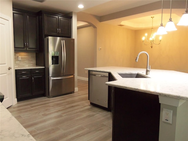 kitchen with arched walkways, a sink, stainless steel appliances, light wood-type flooring, and backsplash