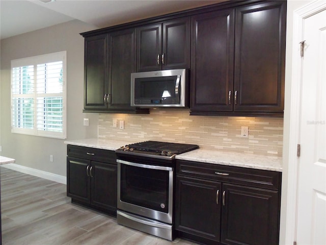 kitchen with tasteful backsplash, baseboards, light stone counters, stainless steel appliances, and light wood-type flooring