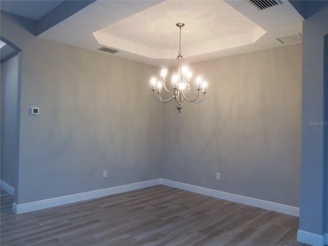 spare room featuring a tray ceiling, visible vents, and wood finished floors