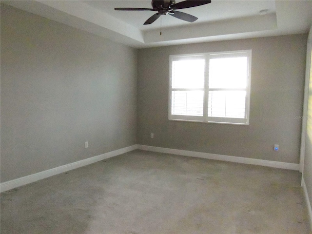 unfurnished room with a tray ceiling, ceiling fan, and baseboards