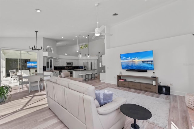 living room featuring ceiling fan with notable chandelier, high vaulted ceiling, and light hardwood / wood-style flooring