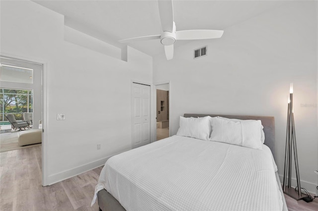 bedroom with ceiling fan, a towering ceiling, light wood-type flooring, and a closet