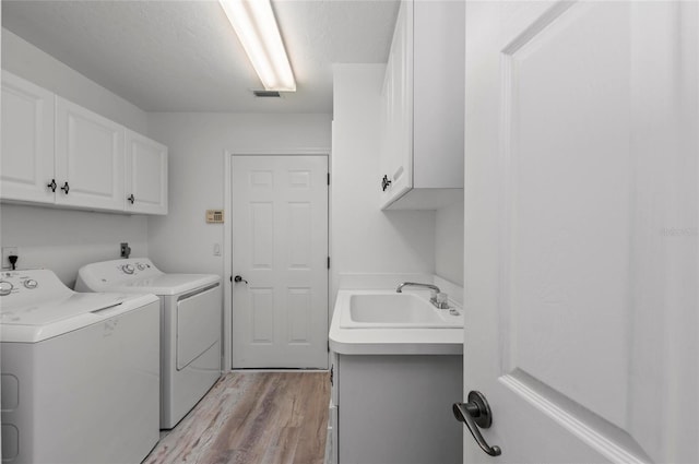 laundry room with sink, cabinets, light hardwood / wood-style flooring, a textured ceiling, and independent washer and dryer