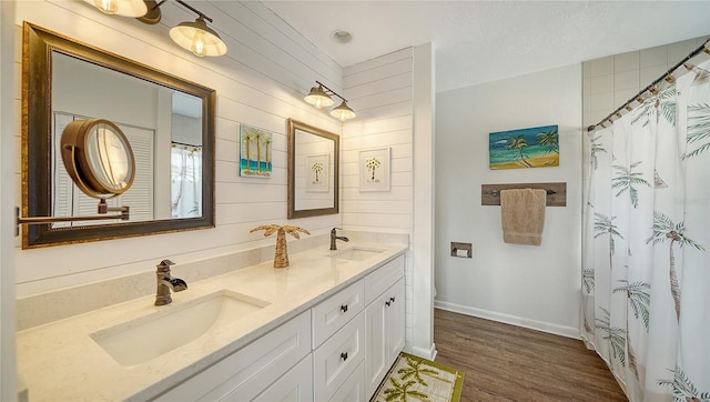 full bath featuring double vanity, a sink, baseboards, and wood finished floors