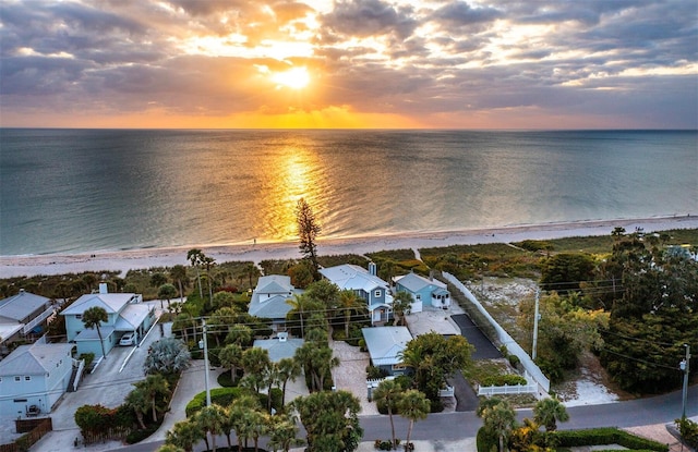 aerial view at dusk featuring a water view and a beach view