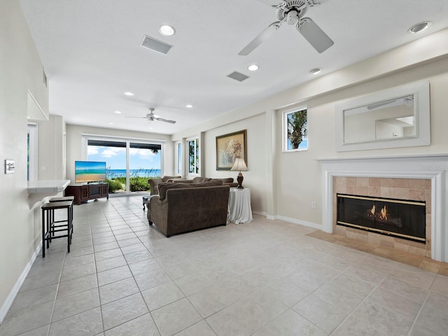 living room with a tile fireplace, ceiling fan, and light tile patterned floors