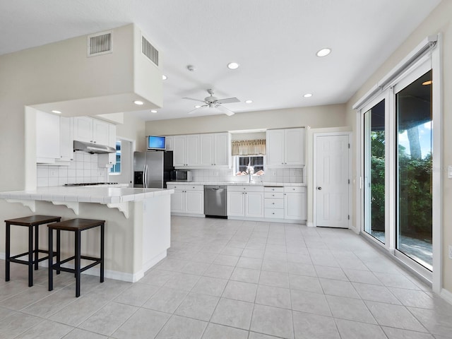 kitchen with a breakfast bar, white cabinets, ceiling fan, appliances with stainless steel finishes, and kitchen peninsula