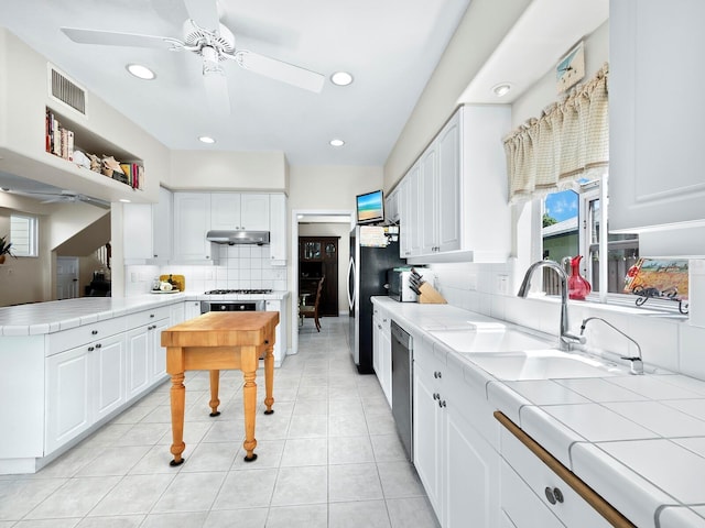 kitchen with tile countertops, stainless steel dishwasher, white cabinetry, and sink