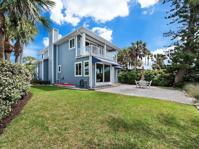 rear view of property featuring a yard, a balcony, and a patio