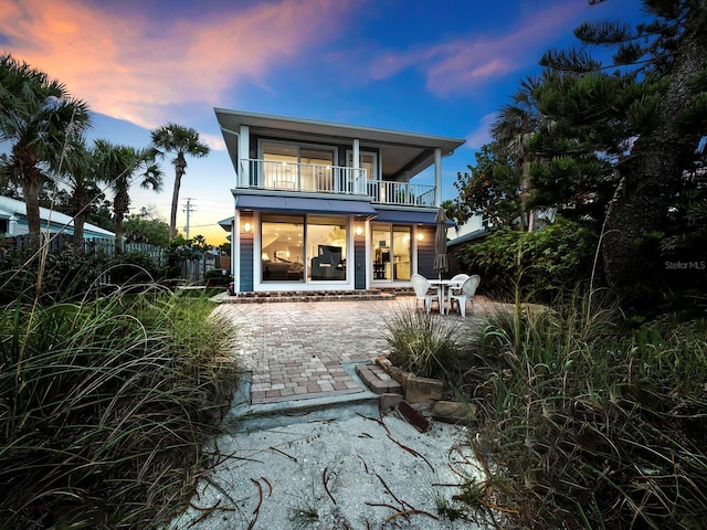 back house at dusk featuring a patio and a balcony