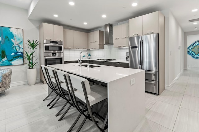 kitchen featuring an island with sink, sink, a kitchen bar, stainless steel appliances, and wall chimney range hood