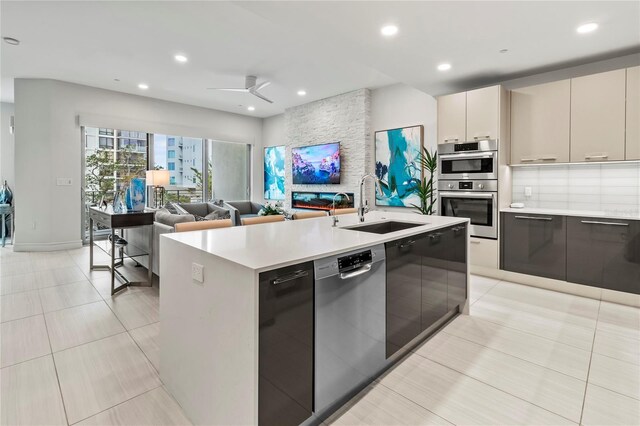 kitchen featuring sink, light tile patterned floors, stainless steel appliances, an island with sink, and decorative backsplash