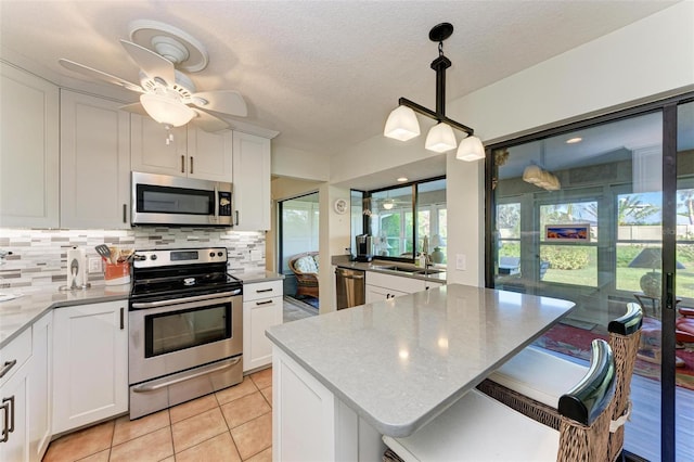 kitchen featuring a center island, appliances with stainless steel finishes, white cabinetry, and decorative light fixtures