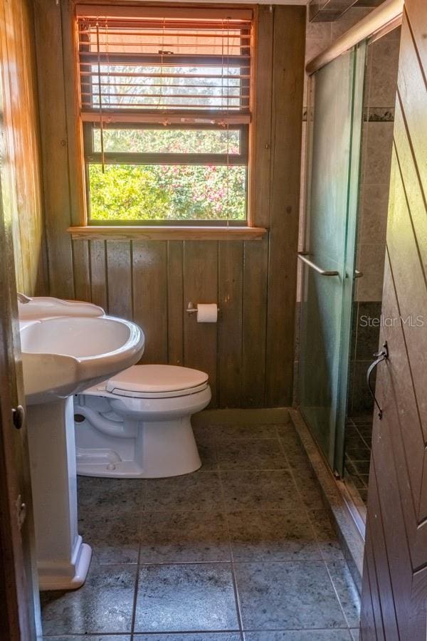 bathroom with toilet, a shower with shower door, and wooden walls