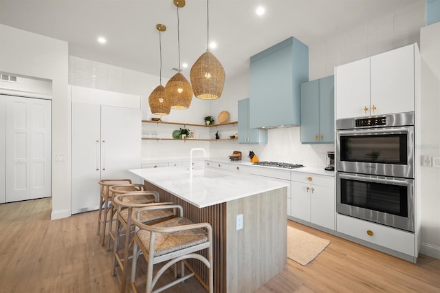 kitchen featuring stainless steel appliances, sink, white cabinets, hanging light fixtures, and an island with sink