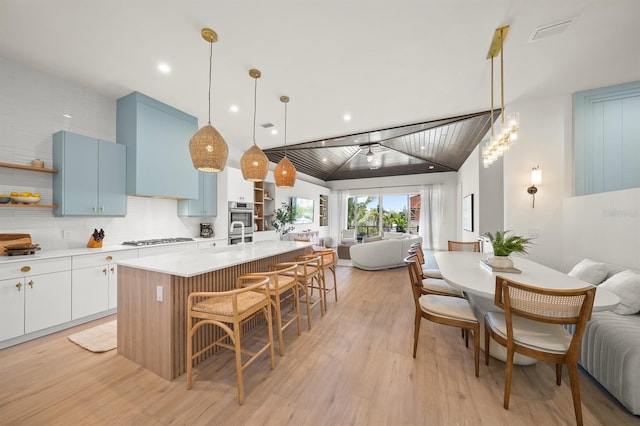 kitchen featuring tasteful backsplash, vaulted ceiling, pendant lighting, white cabinetry, and an island with sink