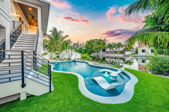 pool at dusk featuring a water view, a yard, and a water slide