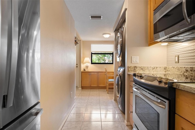 kitchen with stacked washer and dryer, light tile patterned floors, stainless steel appliances, and a textured ceiling