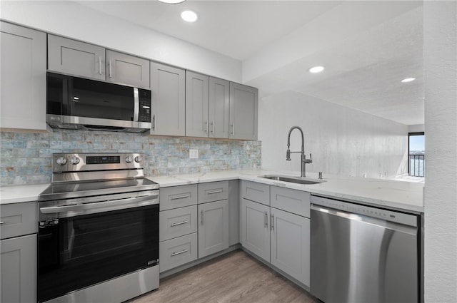 kitchen featuring stainless steel appliances, tasteful backsplash, gray cabinetry, a sink, and light wood-type flooring