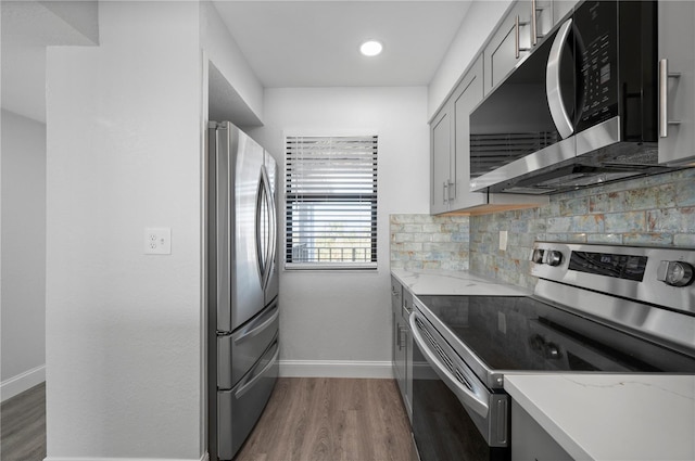 kitchen featuring dark wood-style flooring, stainless steel appliances, backsplash, gray cabinetry, and light stone countertops