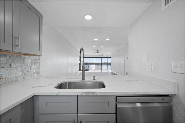 kitchen featuring decorative backsplash, dishwasher, light stone counters, gray cabinets, and a sink