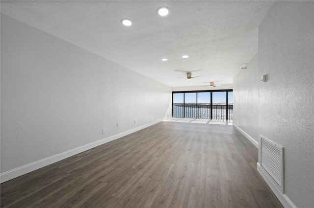 unfurnished room with a textured ceiling, a textured wall, visible vents, baseboards, and dark wood finished floors