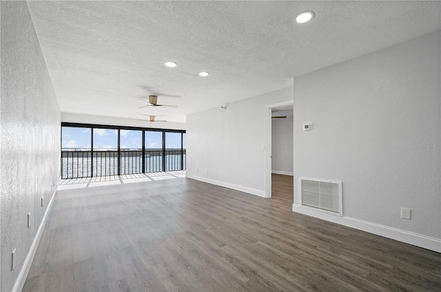 empty room featuring a water view, visible vents, baseboards, a ceiling fan, and dark wood finished floors