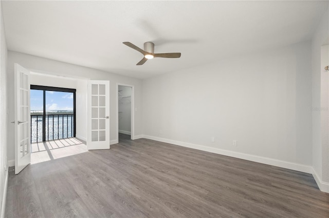 unfurnished room with french doors, dark wood finished floors, a water view, ceiling fan, and baseboards