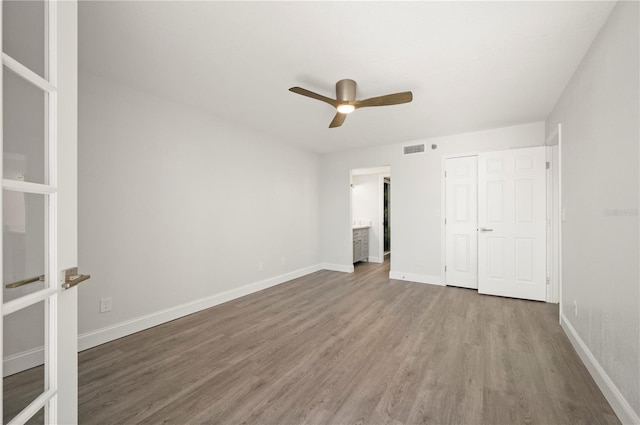 unfurnished bedroom with connected bathroom, wood finished floors, a ceiling fan, visible vents, and baseboards