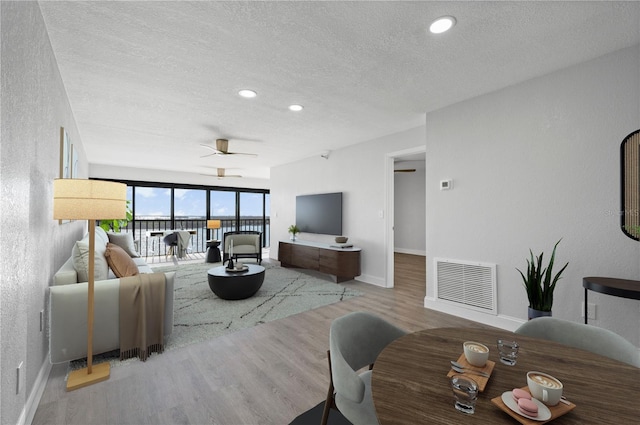 living room featuring light wood-style floors, baseboards, visible vents, and a textured ceiling