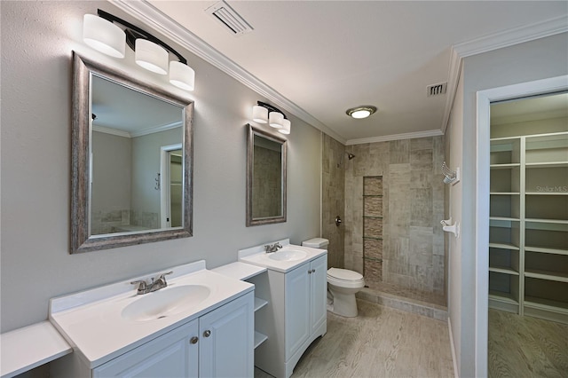 bathroom with vanity, toilet, ornamental molding, a tile shower, and wood-type flooring