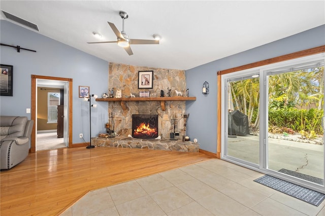 living room with light tile patterned floors, a stone fireplace, vaulted ceiling, and ceiling fan