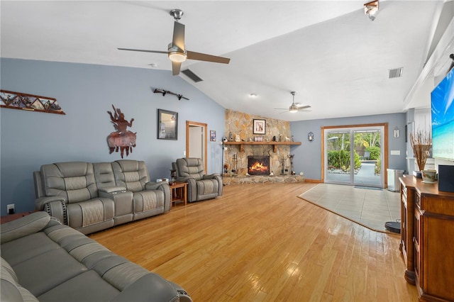 living room featuring ceiling fan, lofted ceiling, a fireplace, and light hardwood / wood-style flooring