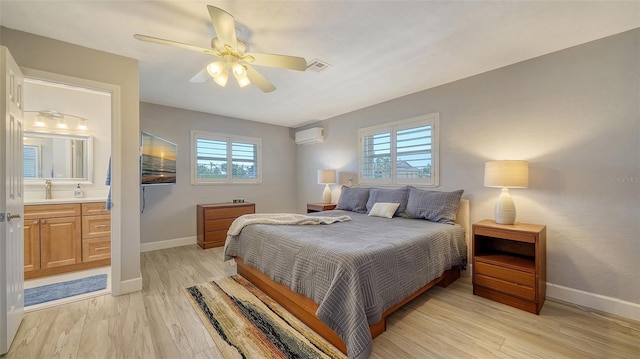 bedroom featuring multiple windows, ensuite bath, a wall unit AC, and light wood-type flooring