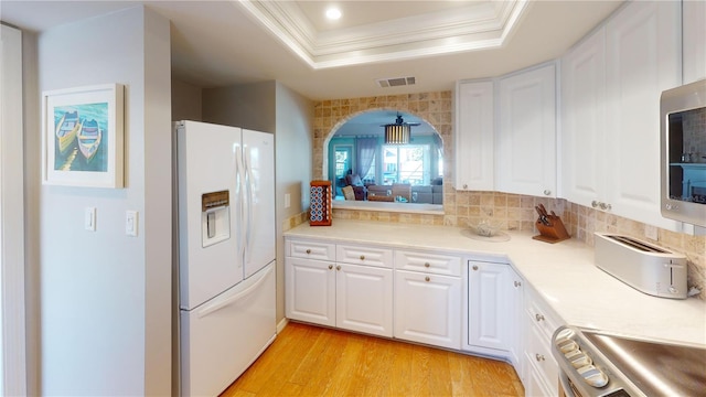 kitchen with ornamental molding, a raised ceiling, white cabinets, range, and white fridge with ice dispenser