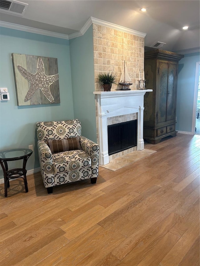 living area featuring hardwood / wood-style floors, crown molding, and a tiled fireplace