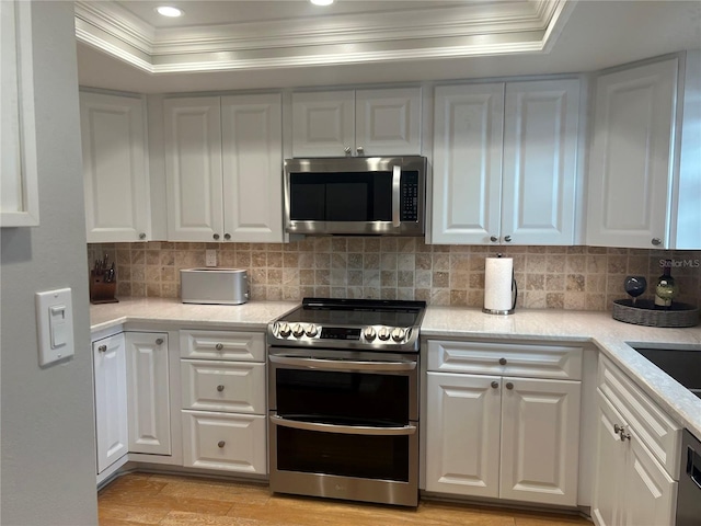 kitchen with backsplash, a tray ceiling, white cabinets, and appliances with stainless steel finishes