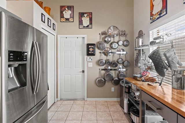 kitchen with butcher block countertops, white cabinets, light tile patterned floors, and stainless steel refrigerator with ice dispenser