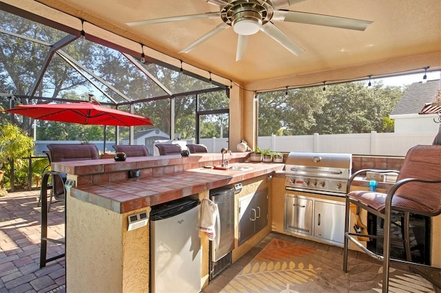 view of patio / terrace with glass enclosure, ceiling fan, exterior kitchen, a grill, and a bar