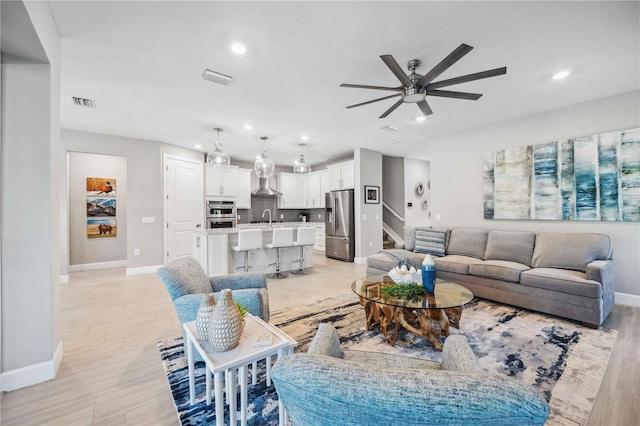 living room featuring ceiling fan, light wood-type flooring, and sink