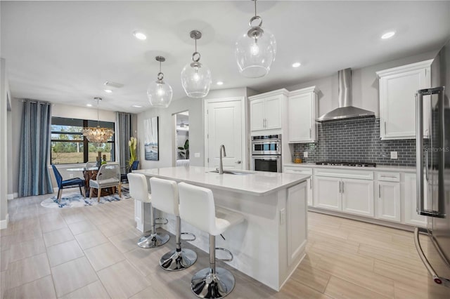 kitchen with white cabinets, hanging light fixtures, wall chimney exhaust hood, and sink