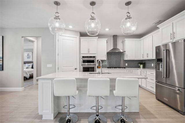 kitchen featuring wall chimney exhaust hood, sink, stainless steel appliances, and a kitchen island with sink