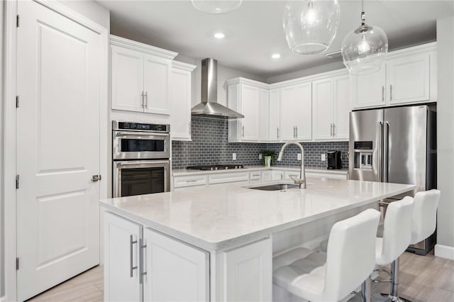 kitchen with white cabinets, a center island with sink, wall chimney exhaust hood, and sink