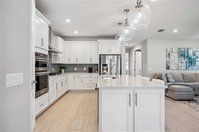 kitchen featuring tasteful backsplash, stainless steel appliances, sink, white cabinetry, and an island with sink