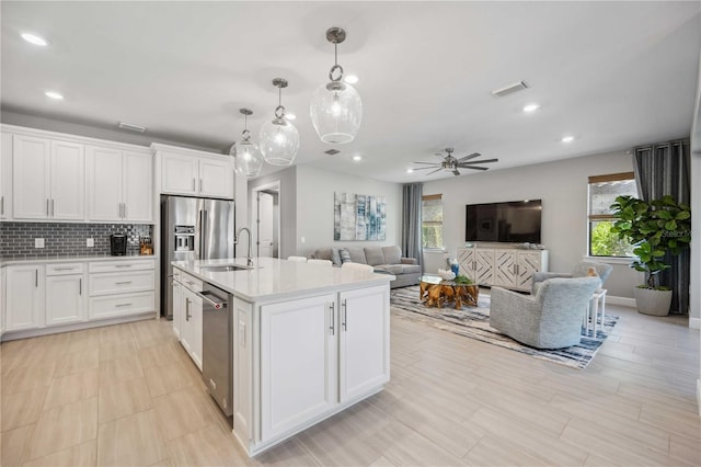 kitchen featuring a kitchen island with sink, white cabinets, sink, decorative light fixtures, and stainless steel appliances