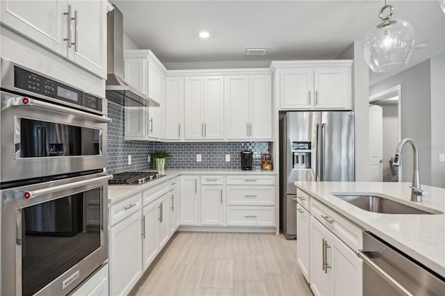 kitchen with wall chimney range hood, sink, tasteful backsplash, white cabinetry, and stainless steel appliances