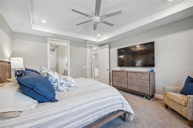 carpeted bedroom featuring a tray ceiling, connected bathroom, and ceiling fan